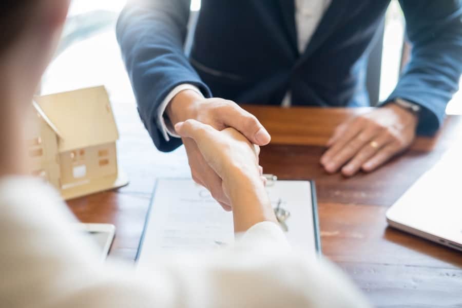 Two people shake hands over a wooden desk and a paper contract.