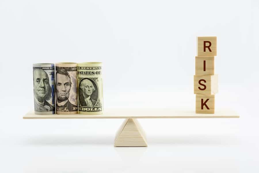 A balance scale shows dollar bills on the left side and wooden blocks that spell "risk" on the right side.