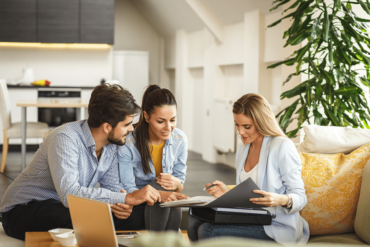 A couple sits inside a home with a business woman looking at a portfolio.