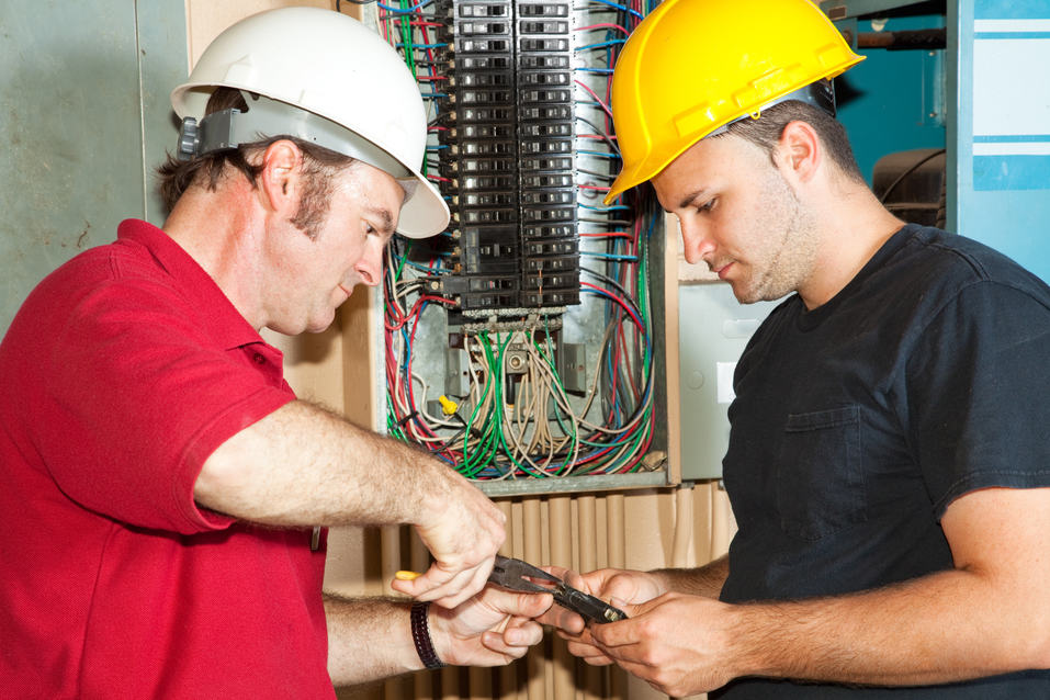 Two people work next to an open electrical box.