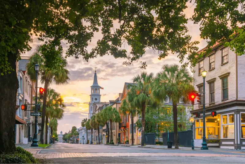 A photo of a main street in South Carolina for a blog discussing Airbnb Laws. The street is cobblestone lined with palm trees and shows building storefronts. The photo appears to be taken early morning at sunrise.