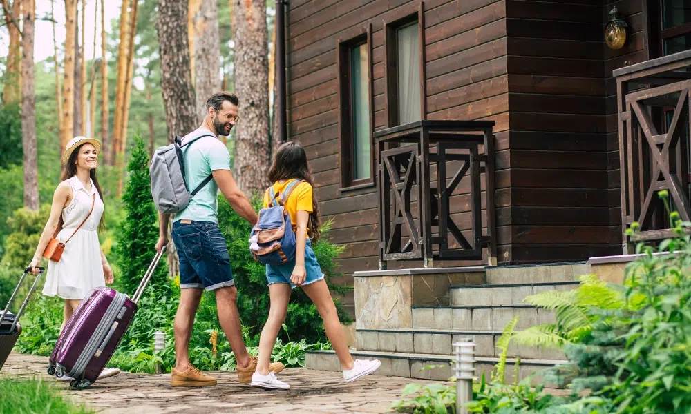 A happy family enters a short-term rental home with their luggage.