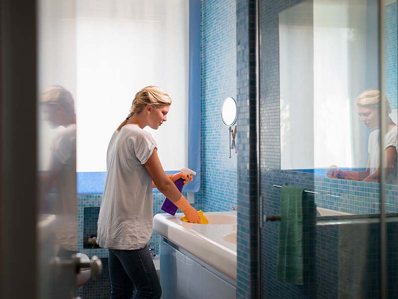 A woman cleans the bathroom in a mid-term rental home.