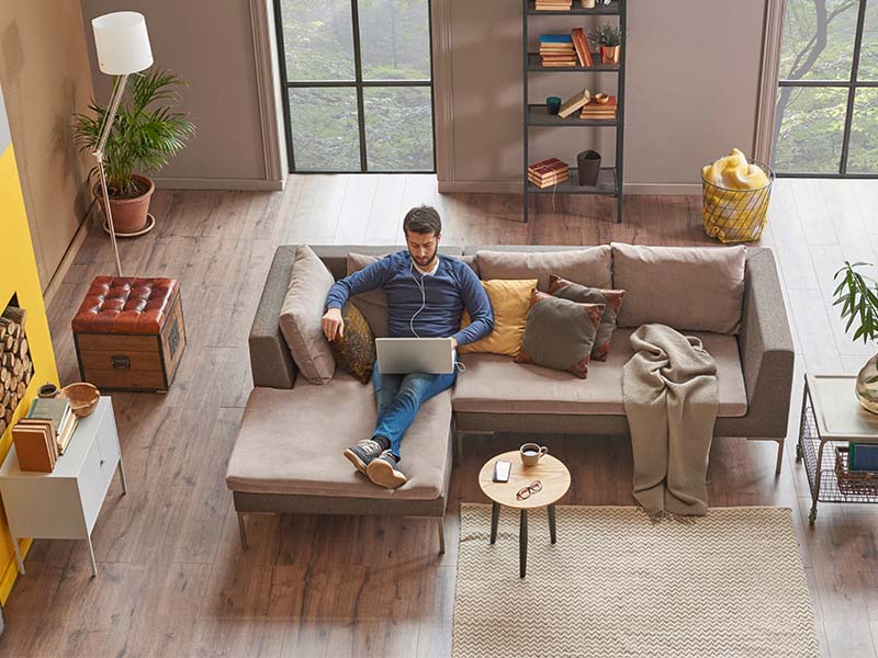 Man sits on a couch looking at a laptop in a modern living space.