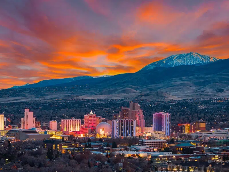 Reno Nevada skyline sits below towering mountains in the distance at sunset