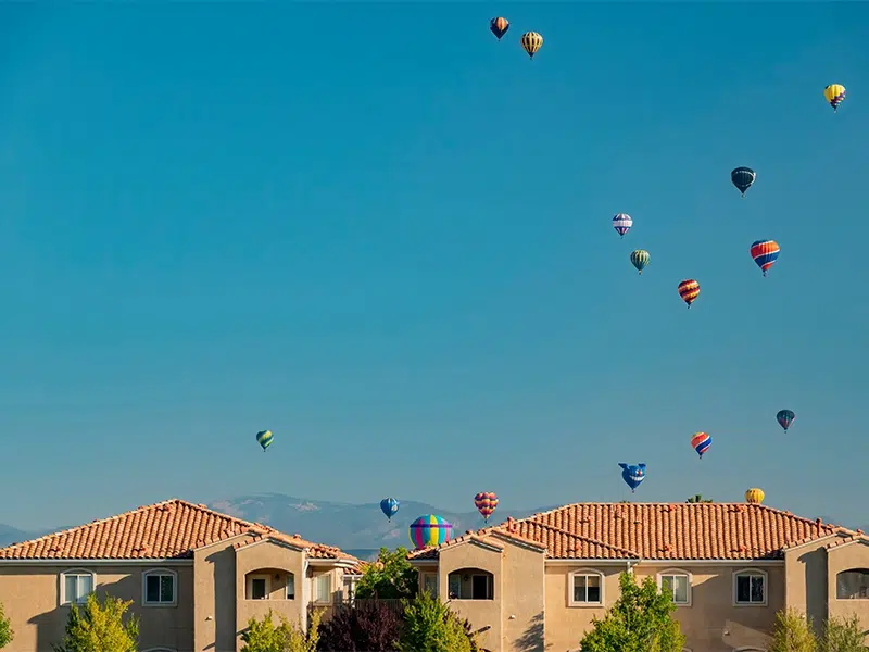 Hot air balloons rising behind the rooflines of homes